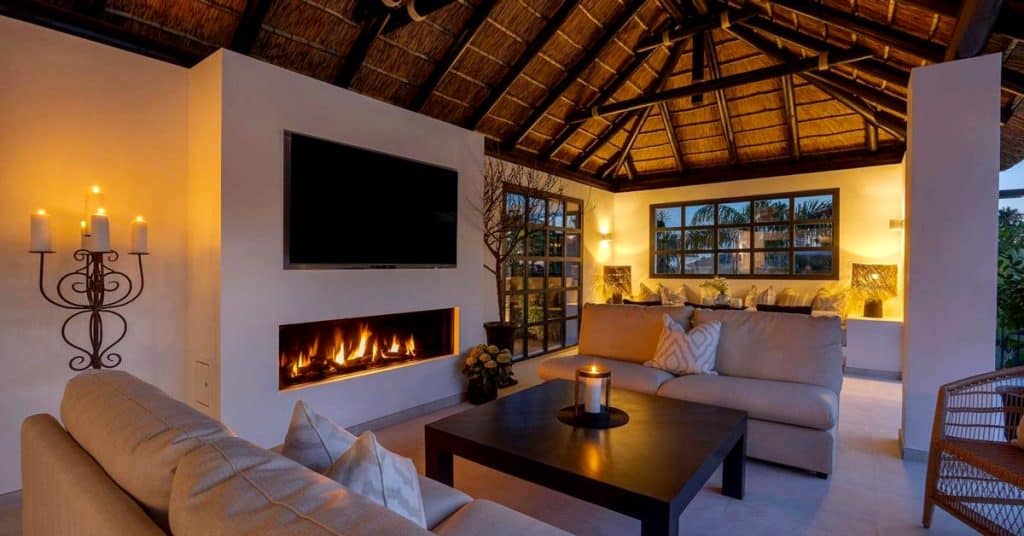 Relaxed boho outdoor living space with soft lighting and a fireplace by the pool