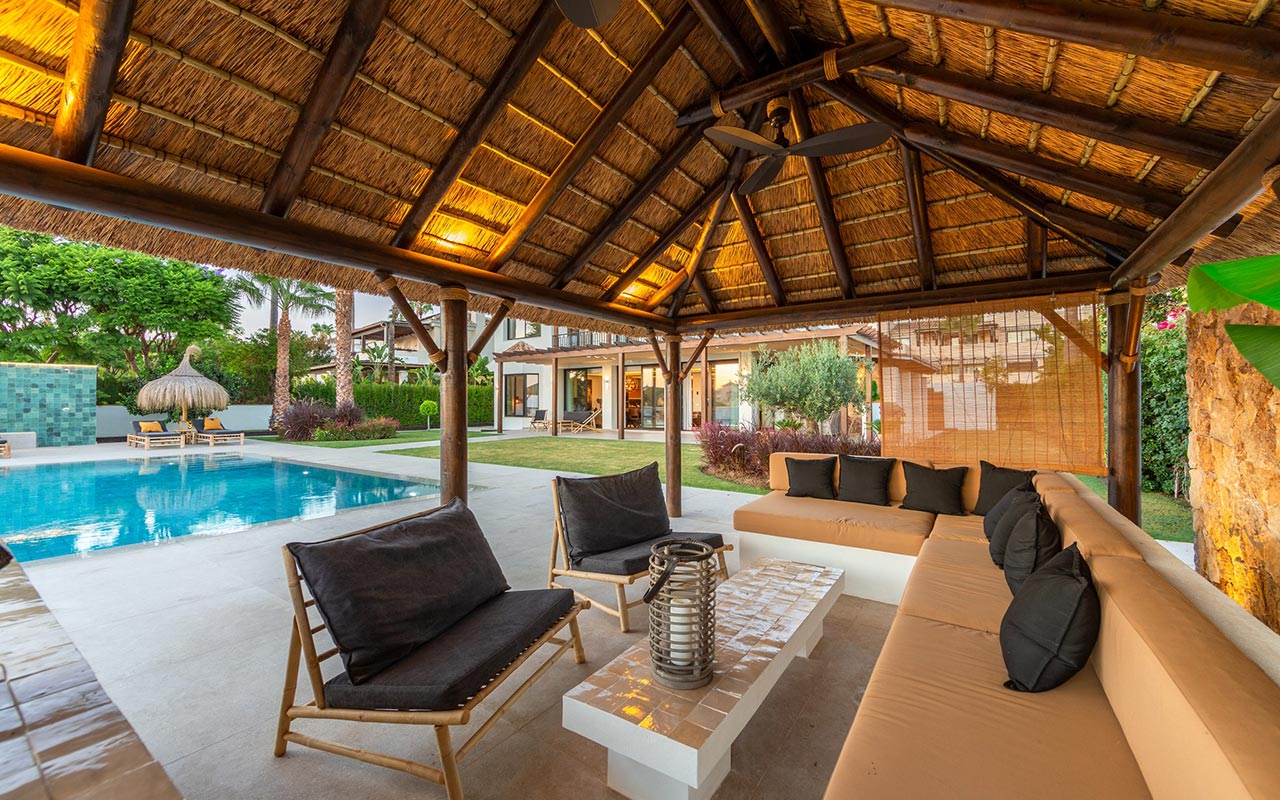 Interior de un gazebo de junco africano en Marbella con techo dorado, vigas de madera, ventiladores y vistas a la piscina